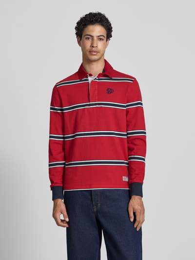 Männermodel trägt Regular Fit Poloshirt mit Logo-Stitching von Superdry in Rot mit weißen und blauen Streifen, Reine Baumwolle, Polokragen, kurze Knopfleiste, Label-Details, Rückenlänge bei Größe M 71 cm, Ganzkörperansicht von vorne.