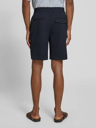Męski model nosi szorty z elastycznym pasem model 'Samos' od Casual Friday, mieszanka materiałów z dodatkiem wiskozy, krój regular fit, szerokość w rozmiarze M 40 cm, długość wewnętrzna nogawki 21 cm, kolor granatowy, gładka tekstura, widok całej sylwetki z tyłu