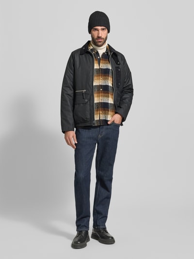 Männermodel trägt Regular Fit Hemdjacke aus reiner Baumwolle Modell 'WOODFOOT' von Barbour mit Optik: Allover-Muster, Gitterkaro, Label Patch, Hemdkragen, einreihige Knopfleiste, Langarm und Manschette, Materialverarbeitung Strick, Farbe in gedeckten Braun- und Gelbtönen, gerade Form, glatte Textur, Ganzkörperansicht von vorne.