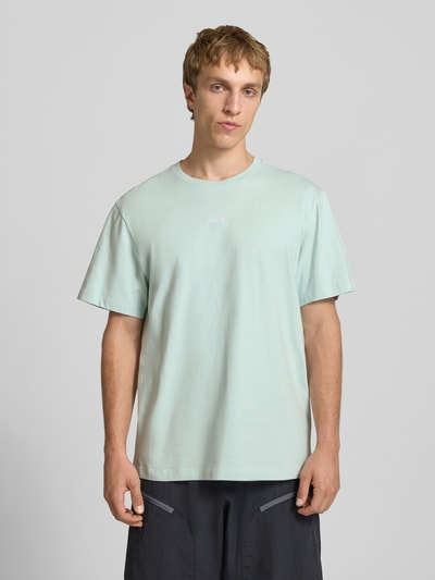 Männermodel trägt T-Shirt mit Logo-Stitching von The North Face in hellgrün, reine Baumwolle, gerader Schnitt, Nahaufnahme Oberkörper.