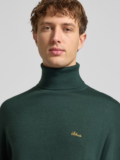Männermodel trägt Loose Fit Rollkragenpullover aus Woll-Mix von BLKVIS in Dunkelgrün mit Label-Stitching, Nahaufnahme Oberkörper. Rückenlänge 68 cm, Ärmellänge 57 cm.