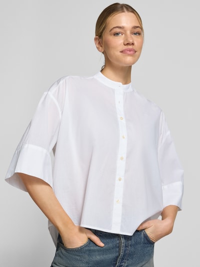 Modelka kobieca nosi Boxy Fit Bluse mit Stehkragen und 3/4-Arm od Emily Van den Bergh, biała bawełna, krój boxy fit, guzik, długość tyłu 68 cm, długość rękawa 29 cm, zbliżenie na górną część ciała z przodu.