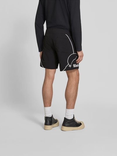 Männermodel trägt Shorts mit Label-Stitching von RHUDE in Schwarz, elastischer Bund, gerade Passform, Ganzkörperansicht Rückansicht.