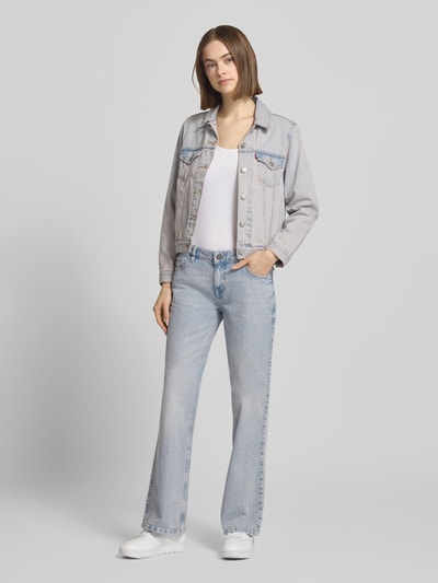 Frauenmodel trägt Bootcut Jeans im Used-Look von Guess Jeans, hellblauer Baumwoll-Elasthan-Mix mit Label-Detail, Ganzkörperansicht von vorne.