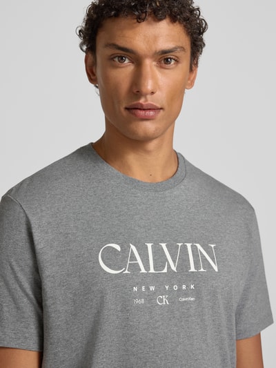 Männermodel trägt T-Shirt mit Label-Print und Rundhalsausschnitt von CK Calvin Klein in Grau, Reine Baumwolle, Regular-Fit, Nahaufnahme Oberkörper.