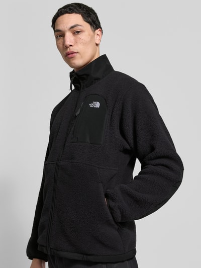 Męski model nosi kurtkę z polaru z napoleońską kieszenią model 'YUMIORI' od The North Face, prosty krój, wpuszczane kieszenie, czarny polar, długość tyłu 70 cm, długość rękawów 70 cm, elastyczne wykończenia, widok z przodu, ujęcie do pasa.