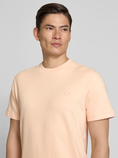 Männermodel trägt Regular Fit T-Shirt aus reiner Baumwolle von Lacoste in Apricot, unifarben, Label Patch, Feinstrick, Nahaufnahme Oberkörper