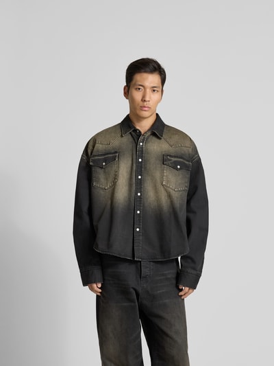 Männermodel trägt Relaxed Fit Jeanshemd im Used-Look von VETEMENTS aus reiner Baumwolle, durchgehende Knopfleiste, Brusttaschen, langärmlig, Rückenlänge 74 cm, Schulterbreite 50 cm, Ärmellänge 74 cm, zweifarbig in Schwarz und Beige, matte Textur, Ganzkörperansicht von vorne.