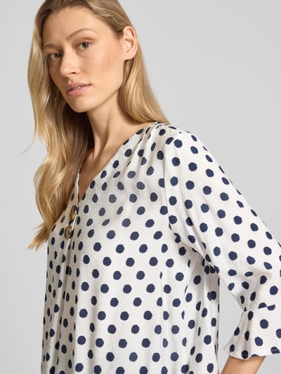 Frauenmodel trägt Blusenshirt mit Viskose-Anteil von Apricot, weiß mit dunkelblauen Punkten, Material-Mix, Nahaufnahme Oberkörper.