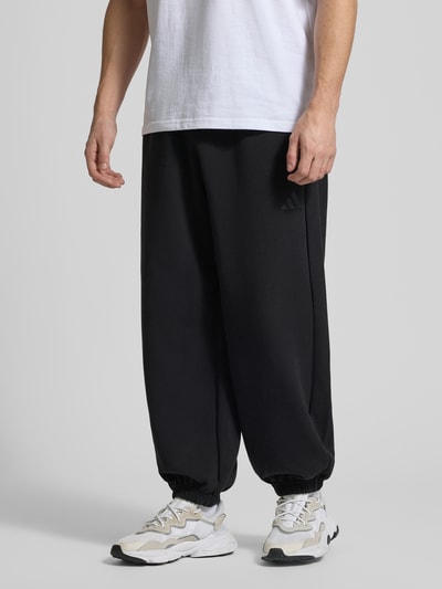 Männermodel trägt Comfort Fit Sweatpants mit Logo-Print von adidas Sportswear, Optik: Unifarben, Materialverarbeitung: Sweat, Ganzkörperansicht von vorne.