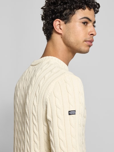 Männermodel trägt Slim Fit Pullover in Strick-Optik von Superdry aus reiner Baumwolle mit Logo-Stitching, Nahaufnahme Oberkörper.