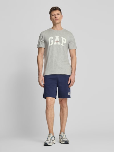 Männermodel trägt T-Shirt mit Logo und Rundhalsausschnitt von GAP, Reine Baumwolle, Regular-Fit, Grauton, Rückenlänge 69 cm, Ganzkörperansicht von vorne.