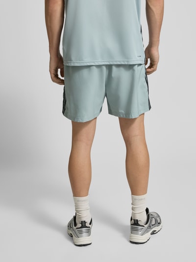 Männermodel trägt Shorts mit elastischem Bund von adidas Training in Hellblau mit schwarzen Streifen, Reißverschlusstaschen, Ganzkörperansicht Rückansicht.
