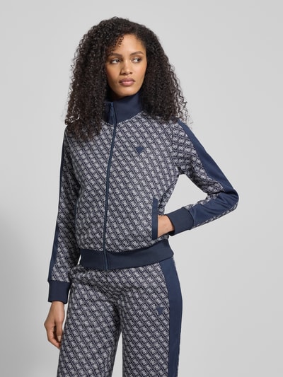 Modelka nosi Sweatjacke mit Stehkragen Modell 'MAYA' od Guess Activewear, regular fit, ciemnoniebieski wzór, zamek, stójka, widok całego ciała z przodu.