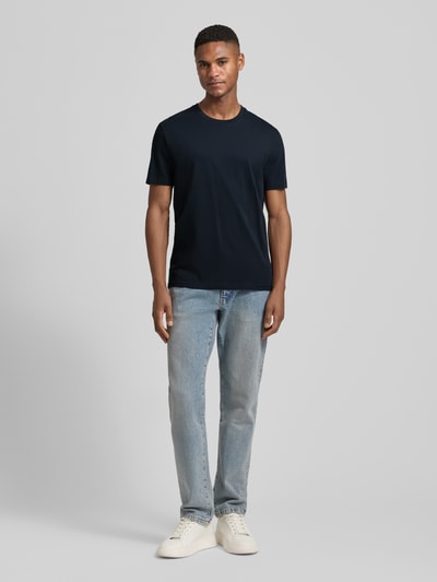 Männermodel trägt T-Shirt mit Rundhalsausschnitt Modell 'DEN' von CINQUE in Dunkelblau zu Jeans, Regular Fit, Ganzkörperansicht von vorne.