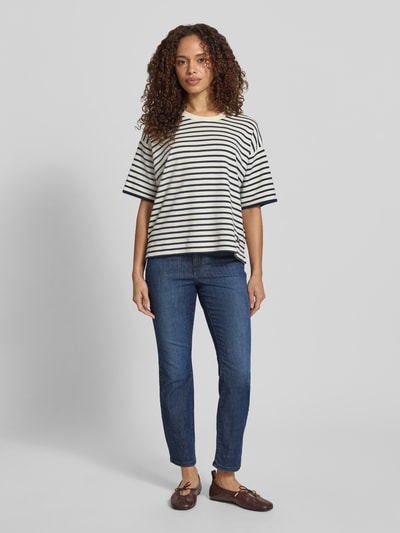 Kobiece model nosi Cropped Slim Fit Jeans mit Eingrifftaschen od Christian Berg Woman z bawełnianą mieszanką ze stretchem, krój slim fit, długość cropped, ciemnoniebieski kolor, skośne kieszenie, szerokość w rozmiarze 36/28: 38 cm, długość wewnętrzna nogawki: 67 cm, pełny widok z przodu.