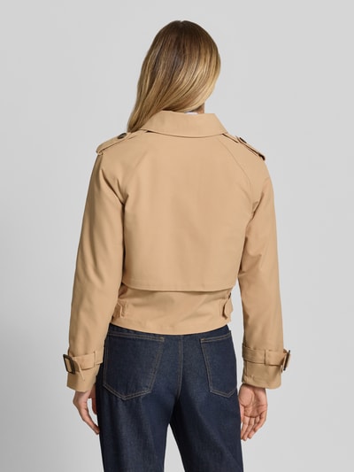 Frauenmodel trägt Trench Jacke mit Eingrifftaschen und Kentkragen von monari in Beige, glatte Textur, Gerader-Schnitt, Ganzkörperansicht Rückansicht. Rückenlänge 52 cm, Schulterbreite 47 cm, Brustweite 47 cm, Ärmellänge 57 cm, Größe 36, doppelte Knopfleiste, Schulterriegel, Ärmelriegel.