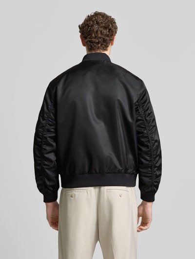 Männermodel trägt schwarze Regular Fit Bomberjacke mit Label-Applikation Modell 'Badam2611' von HUGO aus Twill, wasserabweisend, Ganzkörperansicht Rückansicht.
