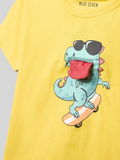 Mädchen trägt T-Shirt mit Rundhalsausschnitt und Motiv-Print von Blue Seven in Gelb, bunte Dino-Grafik, reine Baumwolle, Nahaufnahme Oberkörper.