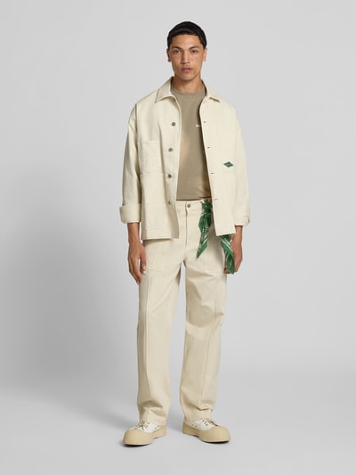 Männermodel trägt Relaxed Fit Jacke in Denim-Optik von Forét in Creme mit Kentkragen, AufgesetzteTaschen, Reine Baumwolle, Ganzkörperansicht von vorne. Rückenlänge 74 cm, Schulterbreite 51 cm, Ärmellänge 67 cm, Größe M.