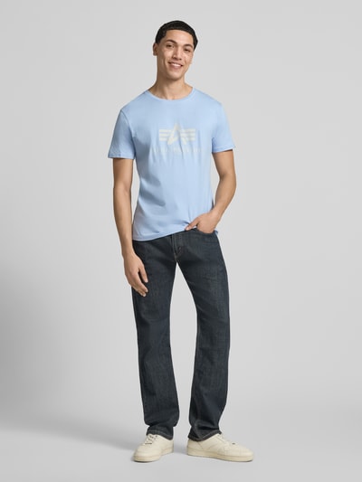 Męski model nosi T-Shirt mit Label-Detail Modell 'BASIC' von Alpha Industries, jasnoniebieski, prosty krój, bawełna, okrągły dekolt, detal z logo, długość tyłu w rozmiarze M: 69 cm, Ganzkörperansicht von vorne.