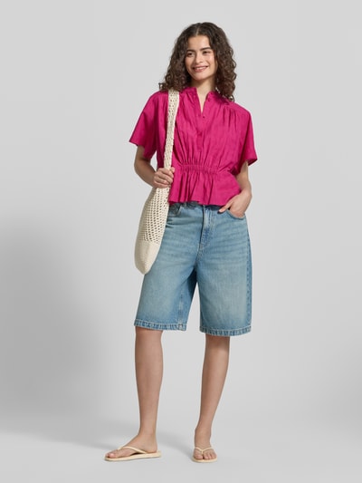 Modelka nosi Boxy Fit Bluse mit Stehkragen und Knopfleiste von Jake*s Casual, bluzka z bawełny w stylizacjach casualowych, różowa, krótkie rękawy, długość tyłu w rozmiarze 38: 54 cm, długość rękawów: 21 cm, jeansowe bermudy, sandały, torba na ramię, jasne tło, całopostaciowy widok z przodu.