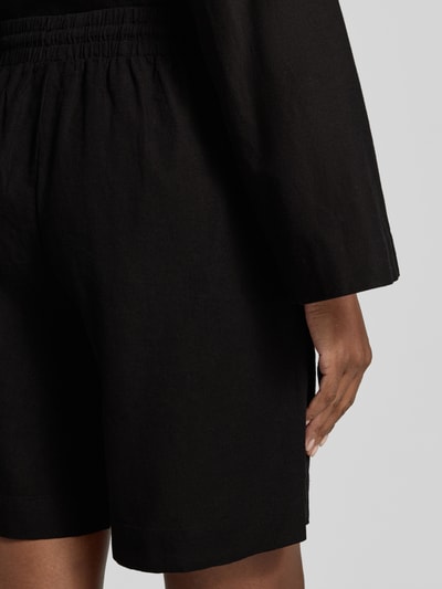 Frauenmodel trägt schwarze Damen Leinenshorts mit elastischem Bund und Kordelzug im Leinen-Mix von FREE/QUENT, Detailaufnahme Rückansicht. Modell 'Lava', Loose-Fit, französische Eingrifftaschen, Bundweite bei Größe S: 39 cm, Innenbeinlänge bei Größe S: 50 cm.