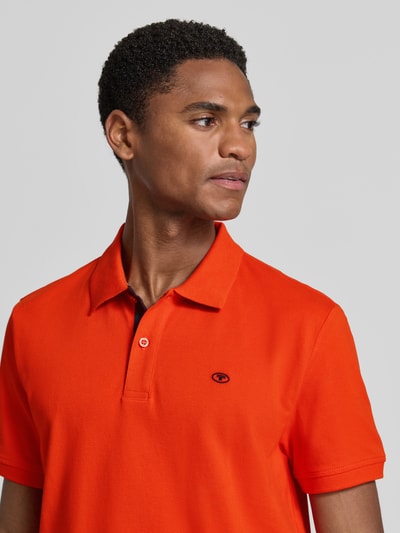 Männermodel trägt Regular Fit Poloshirt aus reiner Baumwolle von Tom Tailor in kräftigem Orange, glatte Textur, Nahaufnahme Oberkörper.
