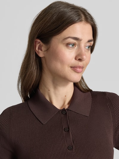 Frauenmodel trägt Slim Fit Poloshirt aus Rippstrick von BOSS in Dunkelbraun mit Polokragen und 3-Knopf-Verschluss, Nahaufnahme Oberkörper.