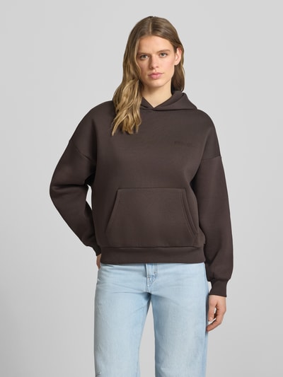 Modelka kobieca nosi Hoodie mit Logo und Känguru-Tasche od Review, mieszanka bawełny, krój relaxed fit, logo, kieszeń kangurka, zdjęcie całej sylwetki z przodu