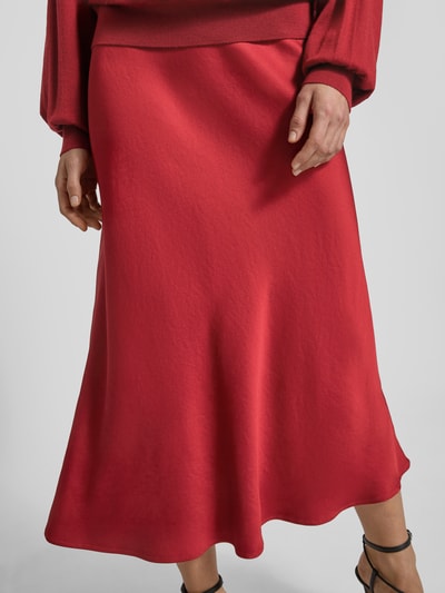 Vrouwenmodel draagt Drykorn Midirock in A-lijn model 'URA', rood, materiaal-mix met stretch, detailopname van de onderlijf.
