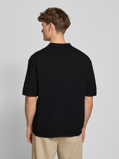 Männermodel trägt Relaxed-Fit Poloshirt Modell 'FERDINAND' von Redefined Rebel aus Reine Baumwolle, Strickshirt, Rückenlänge 70 cm bei Größe M, schwarze Struktur, Ganzkörperansicht Rückansicht.