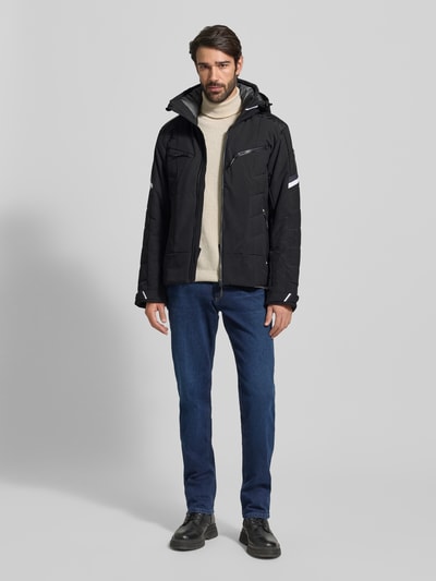 Männermodel trägt Jacke mit Kapuze Modell 'KALDOAIVI' von LUHTA in Schwarz, Regular-Fit, Reißverschluss, Reißverschlusstaschen, Ärmelriegel, Label-Detail; Hosen in Blau, Schuhe in Schwarz, Ganzkörperansicht von vorne.