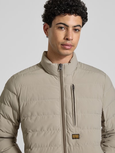 Mannelijk model draagt Regular Fit Steppjacke mit Logo-Patch Modell 'Foundation' van G-Star Raw in beige, gewatteerde look, close-up bovenlichaam.