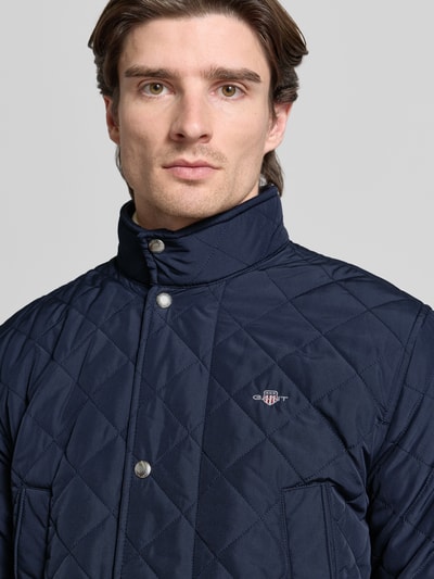 Männermodel trägt Regular Fit Steppjacke mit Logo-Stitching Modell 'Windcheater' von Gant in Dunkelblau, Stepp-Optik, Nahaufnahme Oberkörper.