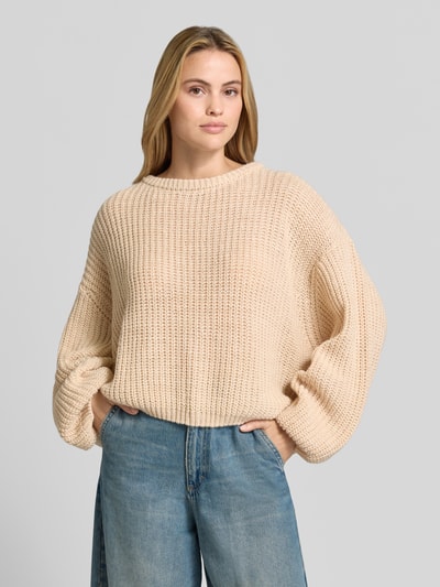Vrouwenmodel draagt Oversized Strickpullover aus Leinen-Mix van American Vintage in beige, linnenmix, oversized, ronde hals, met lange mouwen, ribboorden, trendy schouderpartijen, ruglengte 56 cm, mouwlengte 54 cm, Nahaufnahme bovenlichaam.