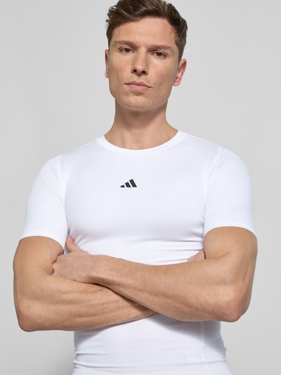 Mannenmodel draagt T-Shirt met Label-Print van adidas Training, slim fit, geribbelde ronde hals, stretchmateriaal, wit, close-up bovenlichaam.