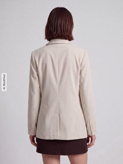 Frauenmodel trägt hellbeigen Loose Fit Longblazer mit steigendem Reverskragen Modell 'NORA' von VERO MODA, strukturierte Oberfläche, Ganzkörperansicht Rückansicht, KI-modifiziertes Bild.
