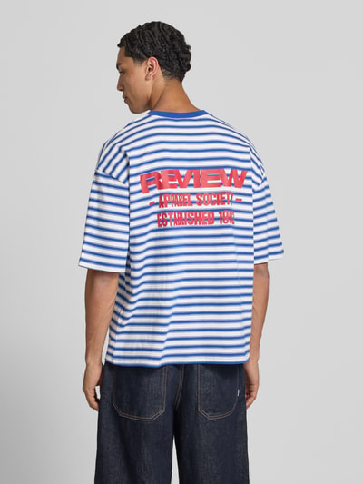 Männermodel trägt Oversized T-Shirt mit Label-Stitching von REVIEW, blau-weiß gestreift, reine Baumwolle, Allover-Look, Rückansicht Ganzkörperansicht.
