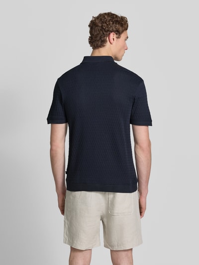 Männermodel trägt Slim Fit Poloshirt mit Reißverschluss Modell 'Franciscojose' von JOOP! Collection aus reiner Baumwolle, Rückenlänge 70 cm, dunkle Farbe, strukturierte Oberfläche, Ganzkörperansicht Rückansicht.