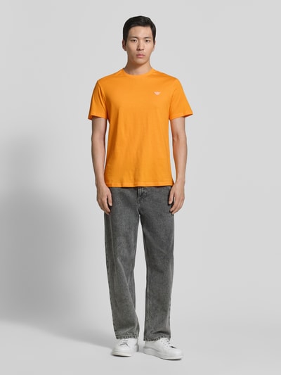 Männermodel trägt T-Shirt mit Logo-Patch und Rundhalsausschnitt von Emporio Armani in Orange, Reine Baumwolle, Modern Fit, Rückenlänge 69 cm, Ganzkörperansicht von vorne.