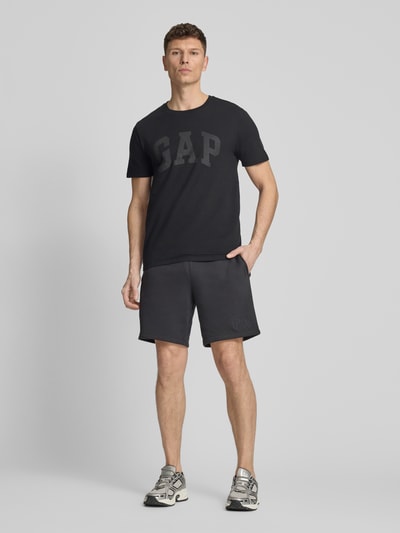 Männermodel trägt T-Shirt mit Logo und Rundhalsausschnitt von GAP, Herren T-Shirt aus Reine Baumwolle, Regular-Fit, Logo, Rückenlänge in Größe M 72 cm, dunkle Farbe, glatte Struktur, Ganzkörperansicht von vorne.