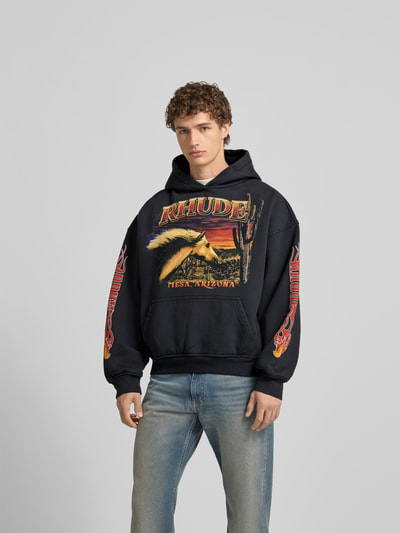 Männermodel trägt Hoodie mit Kapuze von RHUDE aus Reine Baumwolle, Lockerer-Schnitt, Label-Print, Känguru-Tasche, Ganzkörperansicht von vorne. Rückenlänge bei Größe M: 61 cm.