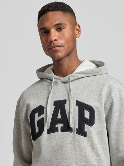 Männermodel trägt Hoodie mit Logo und Känguru-Tasche von GAP in hellgrau, Baumwoll-Mix, Regular Fit, Nahaufnahme Oberkörper.