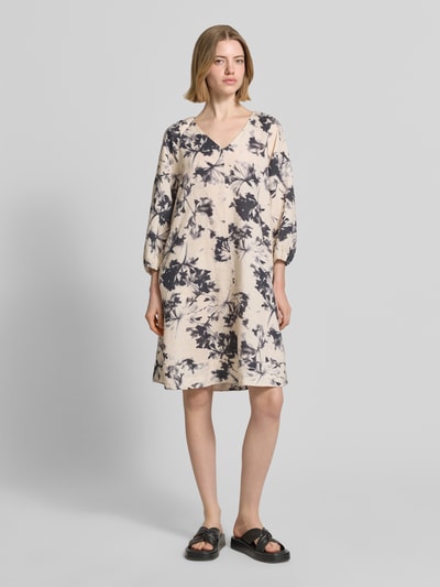 Frauenmodel trägt Fließendes Tunikakleid aus reinem Leinen von Marc O'Polo mit Optik:Allover-Muster, Midi-Länge, V-Ausschnitt, Floral, Kurzarm, Ärmelabschluss elastisch, Flammgarn, Material: Leinen, Beige mit schwarzen floralen Mustern, Ganzkörperansicht von vorne.