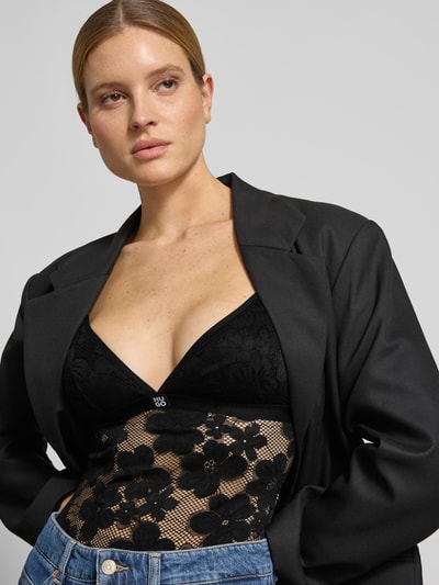 Frauenmodel trägt Wäsche-Body in Spitzen-Optik Modell 'BLOOM LACE BODYSUIT' von HUGO mit Label-Patch, gepolsterten Cups, V-Ausschnitt, verstellbaren Spaghettiträgern, Karree-Rückenausschnitt und Spitze, schwarze Farbe, florale Muster und feine Netzstruktur, Nahaufnahme Oberkörper.