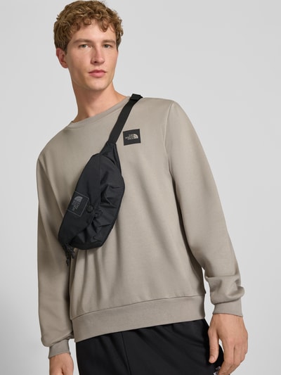 Männermodel trägt Bauchtasche mit Logo-Print Modell 'Glen' von The North Face in Schwarz, Reißverschluss, verstellbarer Schulterriemen, Ganzkörperansicht von vorne.