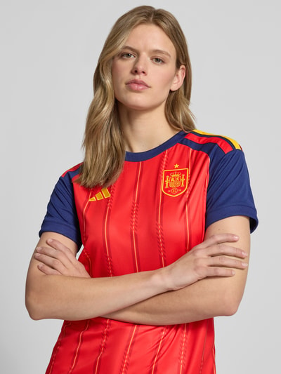 Frauenmodel trägt Spanien Heimtrikot 2026 von adidas Sportswear, Mehrfarbig, Regular-Fit, Logo-Patch, Logo-Detail, Rundhals, Kurzarm, Nahaufnahme Oberkörper.