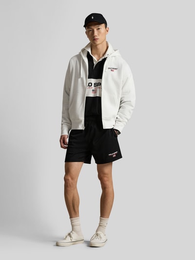 Männermodel trägt Relaxed Fit Sweatjacke aus Baumwoll-Mix von Polo Ralph Lauren in Weiß, unifarben, Reißverschluss, Kapuze, Ganzkörperansicht von vorne.