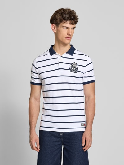 Männermodel trägt Slim Fit Poloshirt mit Label-Stitching und Knopfleiste von Superdry aus Reine Baumwolle, Ganzkörperansicht von vorne. Rückenlänge bei Größe M: 70 cm.